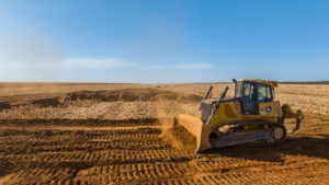 Trator de esteira John Deere da Armac em área agrícola, realizando terraplanagem e movimentação de solo para preparo do terreno